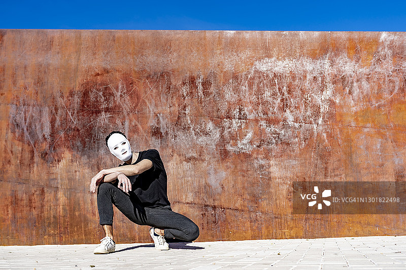 在阳光明媚的日子里，戴着口罩蹲在墙边的男人图片素材