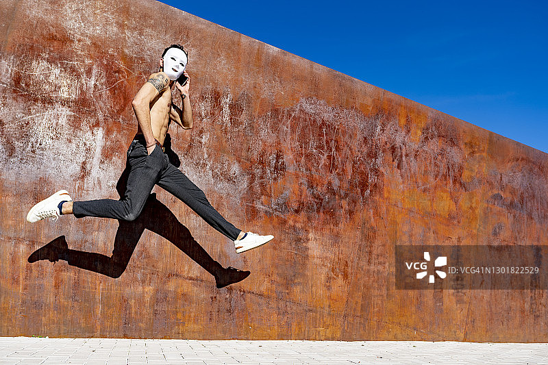 戴着白色面具，靠墙跑步时用手机交谈的男人图片素材