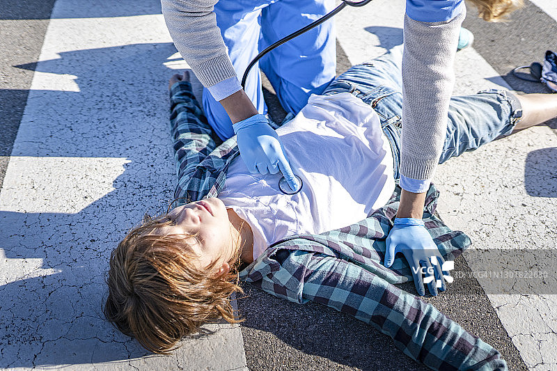 男救援人员用听诊器检查车祸后躺在路上的男孩图片素材