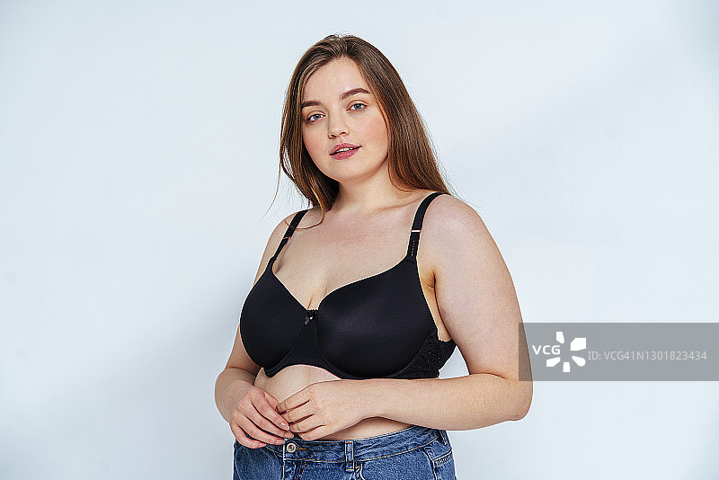 穿着胸罩和牛仔裤、靠在白色背景上的曲线身材时装模特图片素材