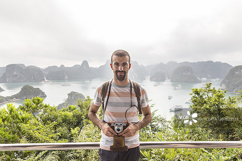 在越南下龙湾的观景点上手持老式相机的微笑男人图片素材