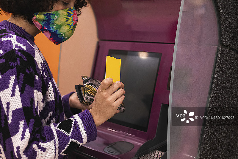 戴着口罩在ATM机上使用信用卡的年轻女人图片素材