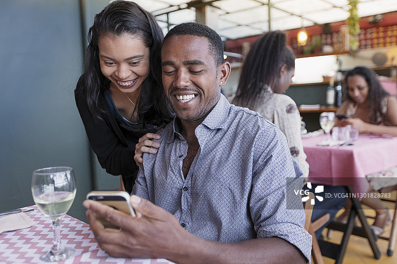 一对黑人和拉丁裔情侣在开放式餐厅里分享手机图片素材