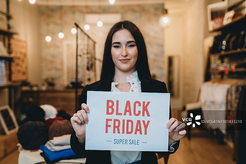 年轻女人在她的商店里拿着“黑色星期五”的标志图片素材