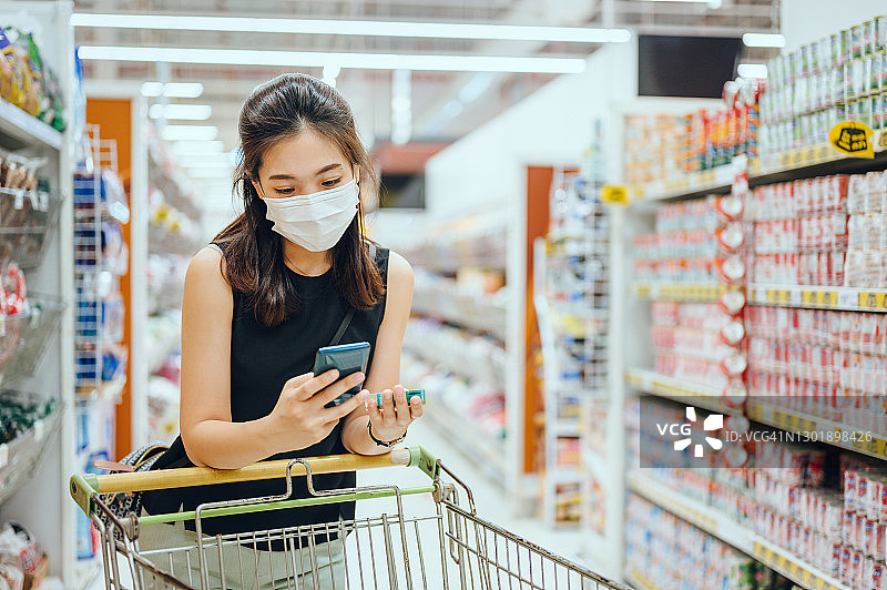 佩戴口罩的年轻亚洲女性在手机上使用信用卡支付图片素材