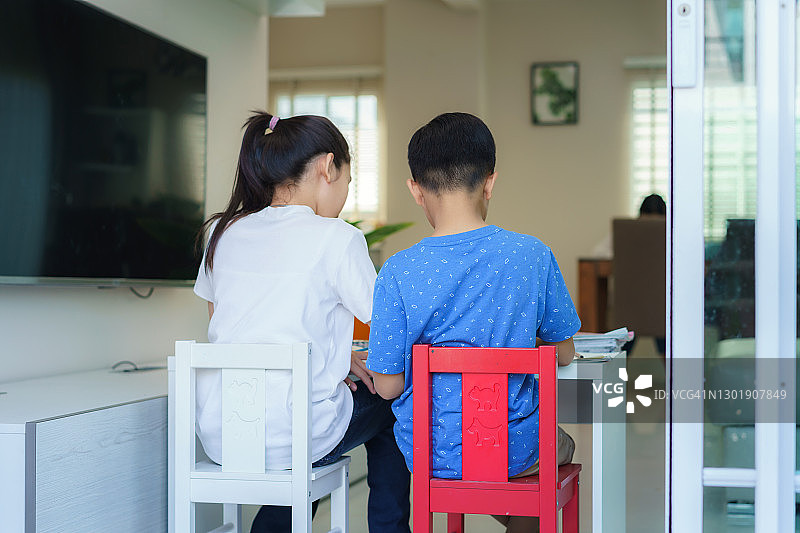疫情期间在家中客厅的桌子上并排做作业的亚洲兄弟姐妹（背影）图片素材