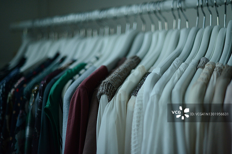 不同颜色的衬衫挂在白色衣架上，按颜色排列图片素材