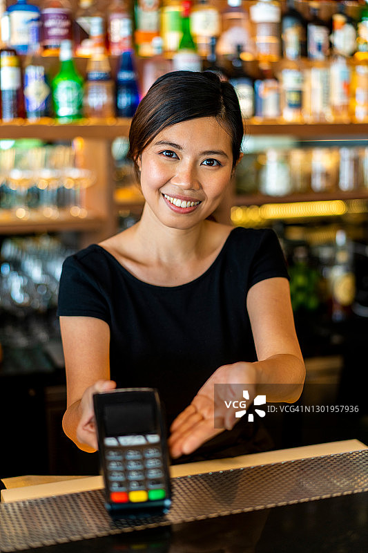 漂亮的亚裔女服务员在餐厅接受无线信用卡支付图片素材