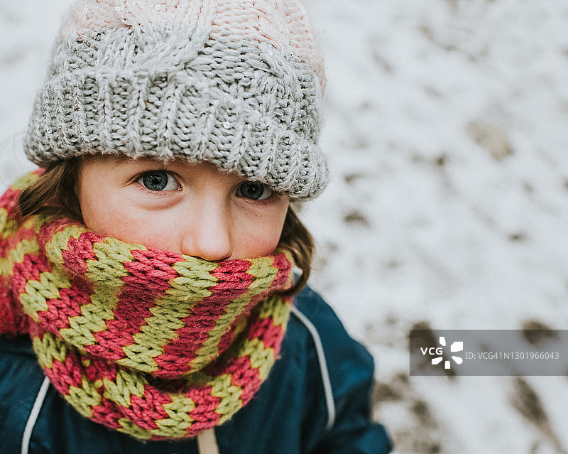 戴着帽子和围巾，眼神闪烁地看着镜头的小女孩图片素材