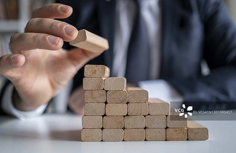 商人在现代办公室抽出或放置木块于塔和半金字塔上，商业中的计划和策略图片素材