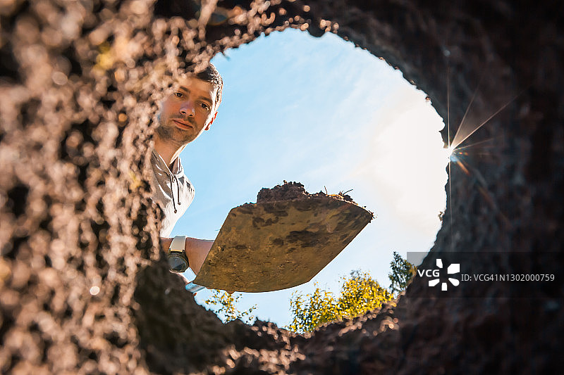 年轻英俊的男人在花园里挖深坑，种植植物和树木图片素材