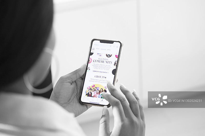 非裔美国妇女在公寓里穿着休闲服看手机上的美容产品网站（肩上视角）图片素材