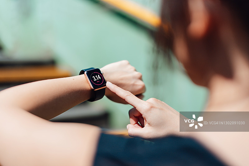 年轻活跃的女性使用智能手表上的运动追踪应用程序来监控跑步后的训练进度的肩上视角图片素材