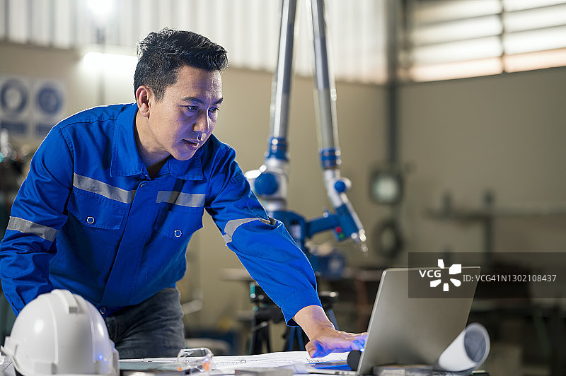 亚洲男工程师在工业机器人手臂中使用笔记本电脑。制造业流程改进思路。图片素材