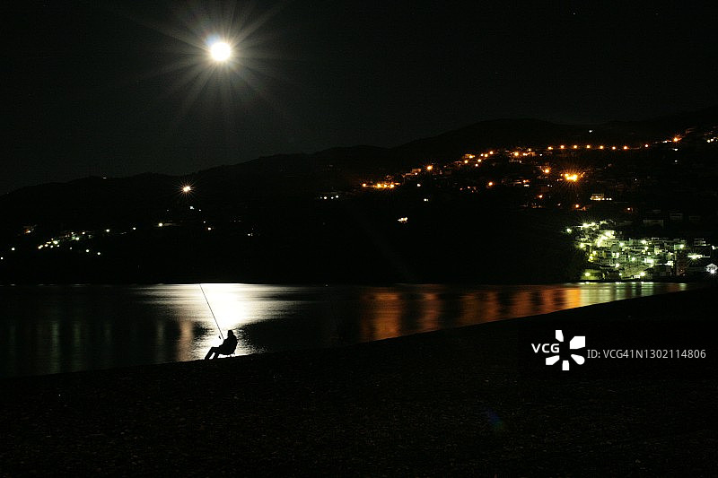 夜晚海边，男人在月光下钓鱼图片素材