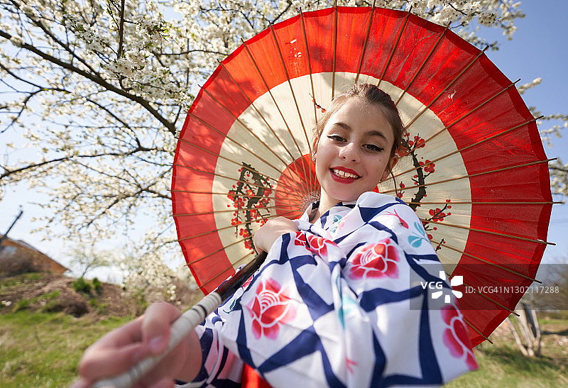 撑伞的微笑女孩身穿传统日式休闲和服，置身樱花树林中图片素材