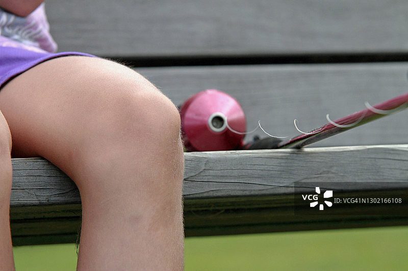 孩子坐在长凳上，腿边放着钓鱼竿图片素材