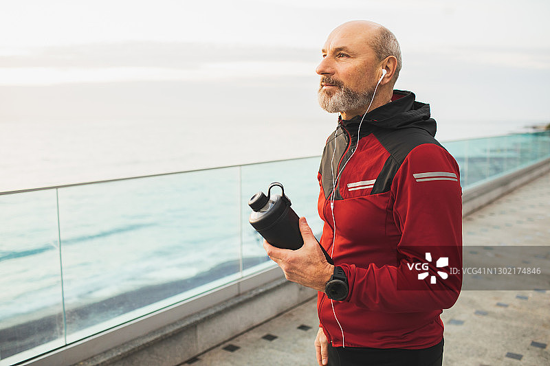穿着运动服、戴着耳机和可重复使用水瓶的成年男性跑步者图片素材