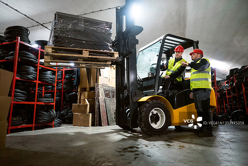 男人在仓库里驾驶叉车，同事向他发出指示图片素材