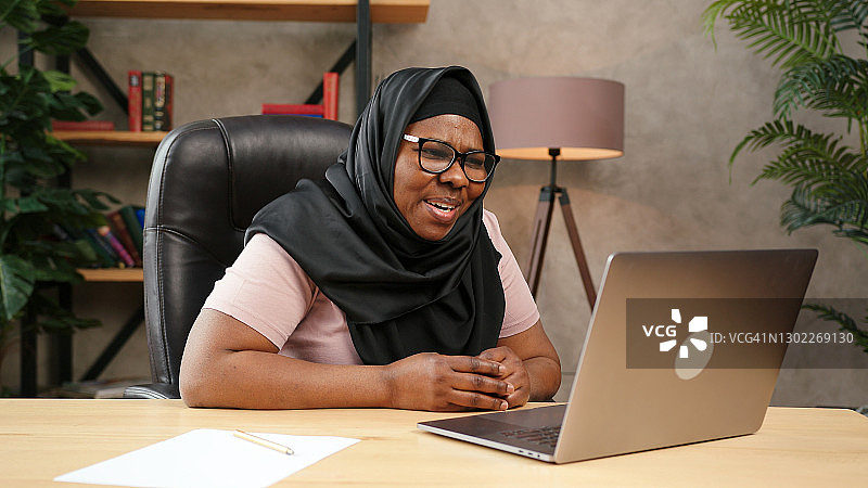 戴黑色头巾的丰满女士看着笔记本电脑屏幕交谈图片素材