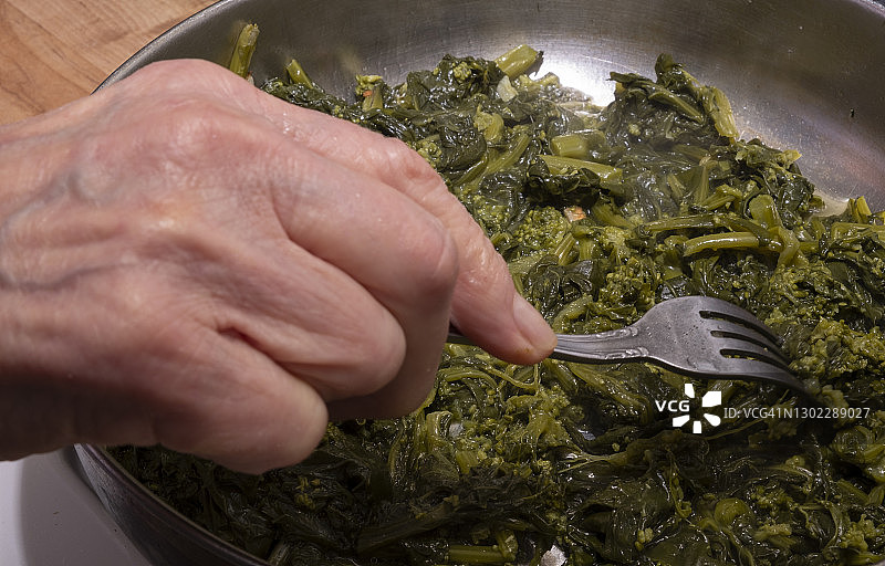 老年妇女的手用大蒜和油在煎锅里炒西兰花图片素材