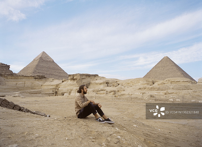 男人坐在吉萨金字塔附近的沙漠中图片素材