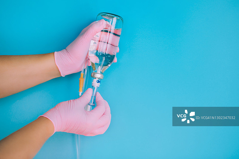 蓝色背景下，戴着粉色手套的医生手中的盐水滴管系统。新冠病毒隔离和医疗概念图片素材