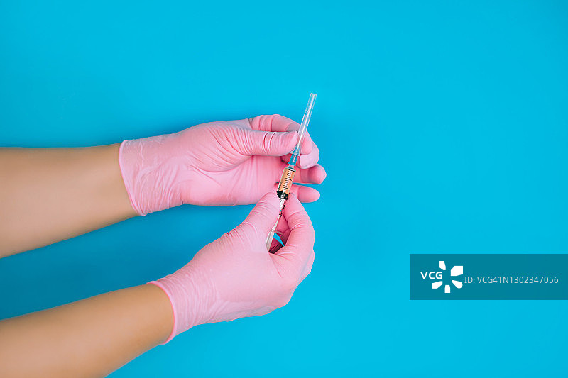 戴粉色手套的医生在蓝色背景下拿着装有冠状病毒疫苗的小注射器图片素材