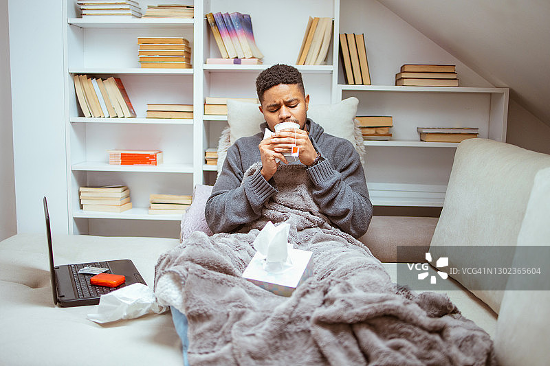 感冒卧床，用手帕擦鼻子的年轻非裔美国男子图片素材