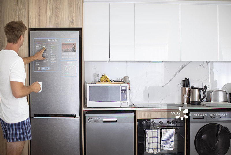 一位成年男子在家中使用冰箱集成的智能家居技术图片素材