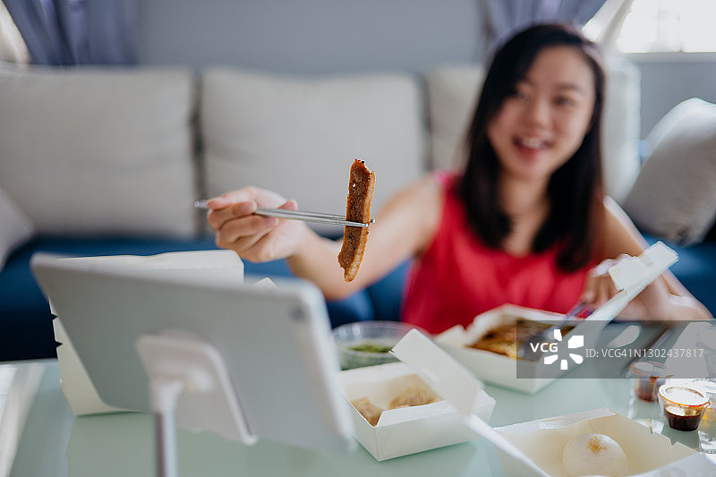 年轻亚洲女性进行视频通话，同时享用外卖食物图片素材
