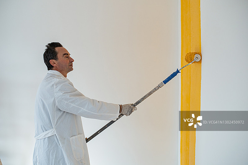 年长的体力劳动者在儿童房墙壁上涂黄色油漆图片素材