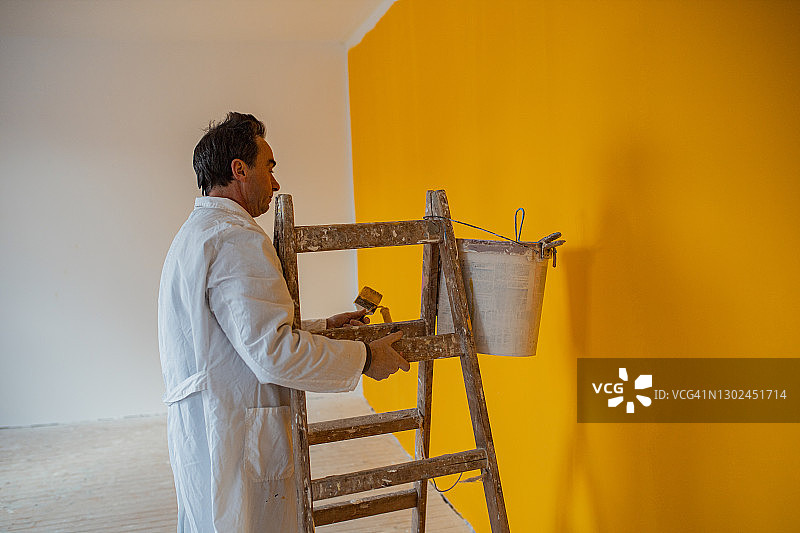 用滚筒将墙壁涂成黄色的年长男人图片素材