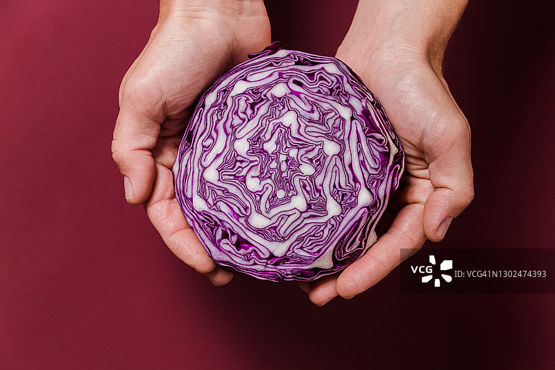 男人手在栗色背景上拿着切好的红色卷心菜。顶视图。文案空间。纯素生食。健康饮食概念。图片素材