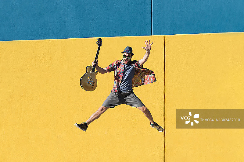 快乐的男音乐家弹着黄色电吉他跳跃演奏流行摇滚音乐图片素材