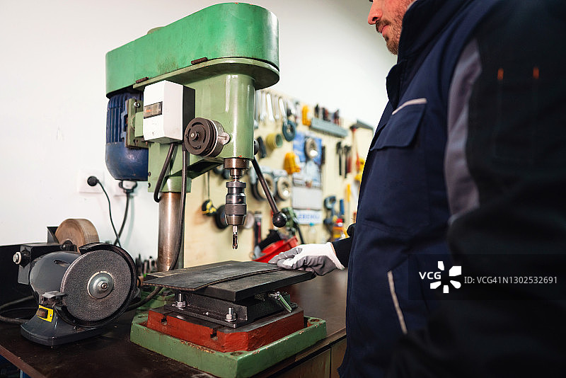 在小型生产线上用钻机工作的年轻体力工人图片素材