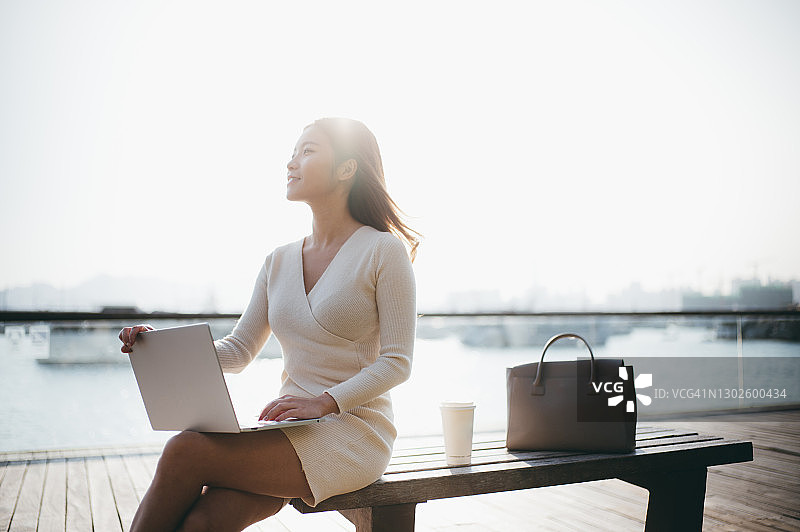 在海滨长廊边使用笔记本电脑的年轻女商人图片素材