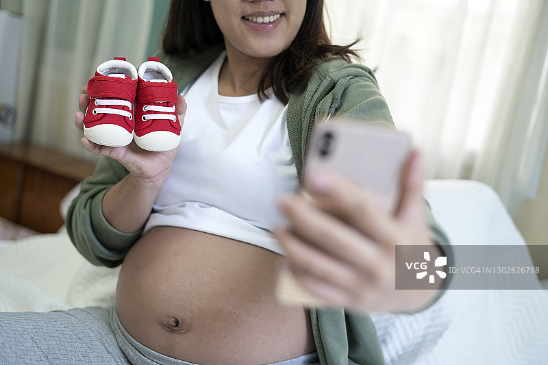 孕妇在卧室用婴儿鞋自拍图片素材