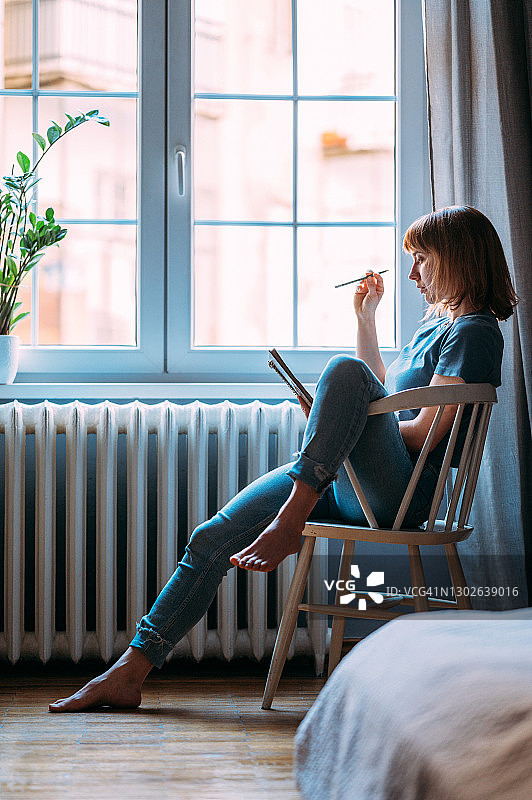 坐在窗边木椅上的年轻棕发女人图片素材