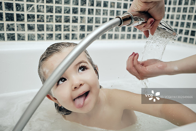 小女孩在浴缸里看着正在给她洗澡的妈妈图片素材