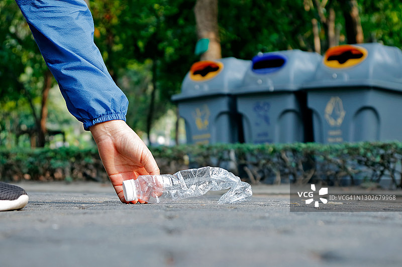 女性捡起地板上的塑料瓶，背景为回收箱图片素材
