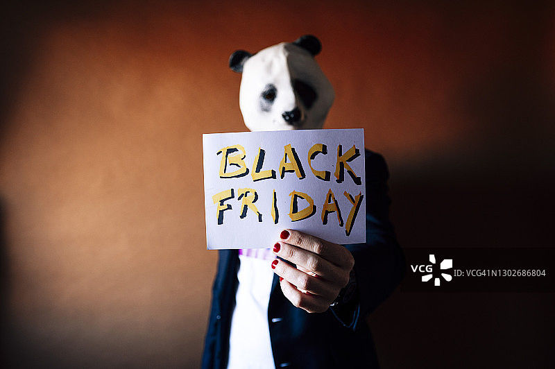 戴着熊猫面具的男人拿着黑色星期五标志图片素材