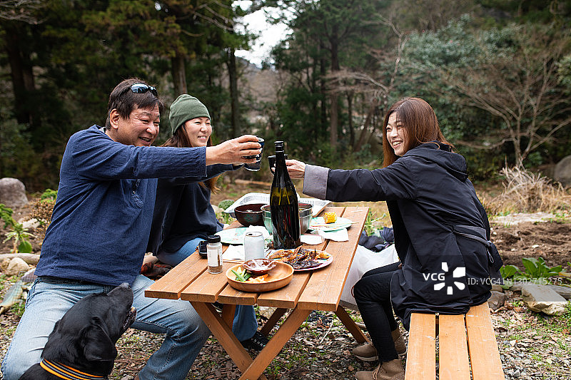 三个朋友在户外餐桌上用餐并举杯祝酒图片素材