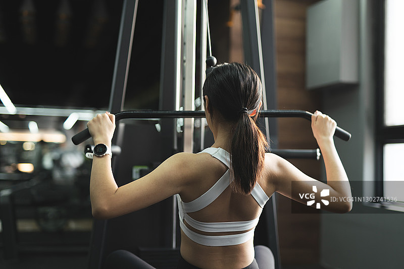 年轻女人在健身房的器械上做背部训练图片素材