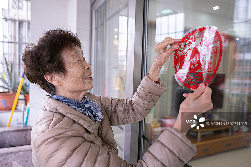 一位年长的中国妇女在家里的玻璃门上粘贴传统的“福”字剪纸，用于中国新年装饰和庆祝图片素材