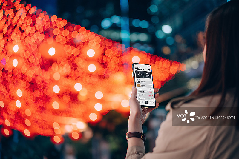 年轻亚裔女性在城市街道上用手机App管理在线银行的肩部视角图片素材