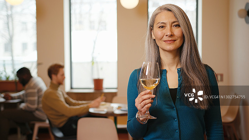 在咖啡馆里手持白葡萄酒的乐观亚洲老年妇女图片素材