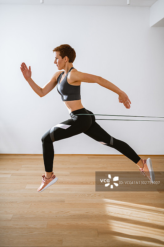 使用阻力带高抬腿跑步的坚定的活跃女性，侧视图图片素材