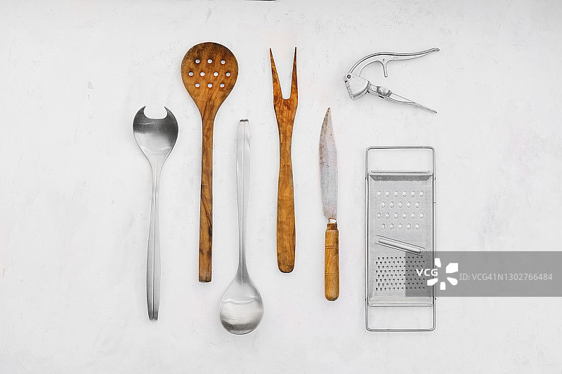 一些复古厨房用具的俯视图——铁制和木制刀具、木制撇沫器和叉子、金属勺子、磨碎器和蒜末粉碎机，白色背景，留有复制空间。图片素材