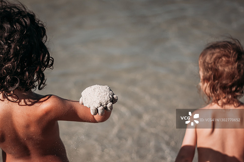 在海滩上的两个孩子，其中一个拿着沙球准备扔图片素材